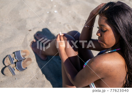 水着で砂浜に座る黒人系カナダ人の女性とサンダル 水着で砂浜に座る黒人系カナダ人の女性とサンダル 77623040