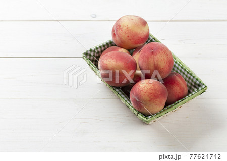 Fresh, ripe peaches in a basket on a white wooden background. Fresh, ripe peaches in a basket on a white wooden background. 77624742