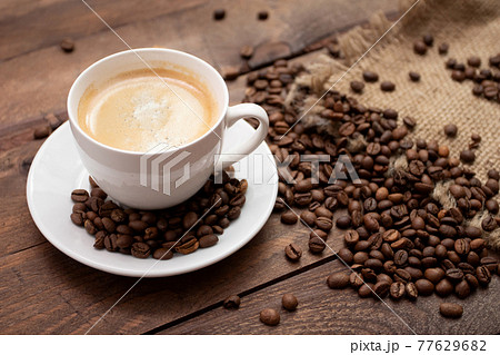 Cup of freshly brewed coffee on wooden table with roasted coffee beans on wooden background Cup of freshly brewed coffee on wooden table with roasted coffee beans on wooden background 77629682