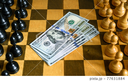 Dollar bills between chess pieces rows on chessboard 77631884