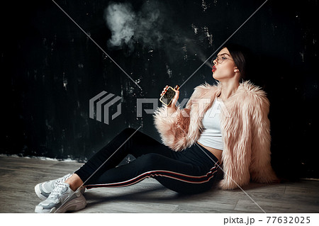 Sexy trendy rap woman in pink fur coat smoke electronic cigarette. Pink Studio background shooting 77632025