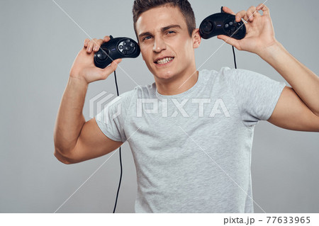 A man with controllers in his hands near his head technology video games entertainment light background A man with controllers in his hands near his head technology video games entertainment light background 77633965