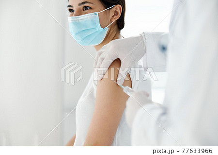 doctor in protective gloves injects a vaccine into the shoulder of a woman patient covid vaccination 77633966