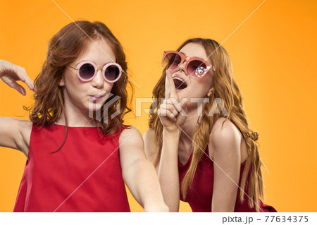 Happy sisters in red dresses on a yellow background are having fun and gesticulating Copy Space 77634375