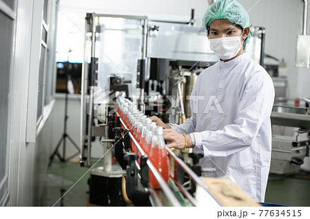 Hygiene worker working in drink factory at conveyor belt with fruit juice glass bottled in production line. 77634515