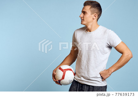 Happy guy with soccer ball in hand on blue background plays soccer cropped view Happy guy with soccer ball in hand on blue background plays soccer cropped view 77639173