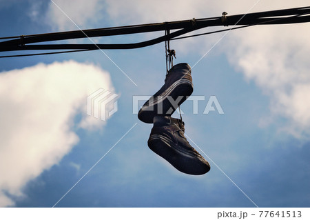 Two dirty old sneakers hanging on wires in blue sky with clouds Two dirty old sneakers hanging on wires in blue sky with clouds 77641513