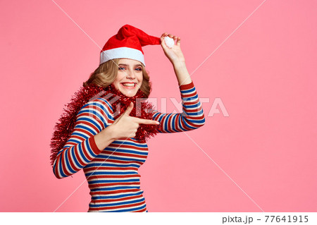Woman with tinsel around her neck and with a cap on her head on a pink background cropped view Woman with tinsel around her neck and with a cap on her head on a pink background cropped view 77641915