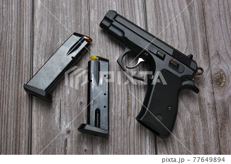 Still life with black handgun with cartridge magazine and dummy bullet on old grungy brown wooden background, Black semi-automatic pistol on wood table 77649894