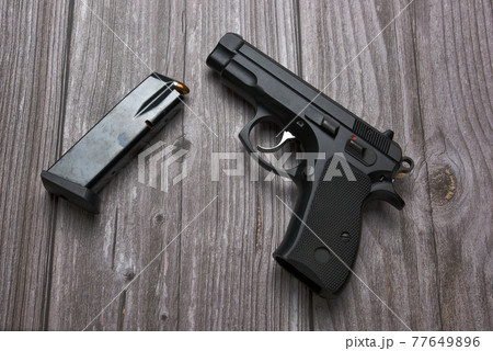 Still life with black handgun with cartridge magazine on old grungy brown wooden background, Black semi-automatic pistol on wood table 77649896