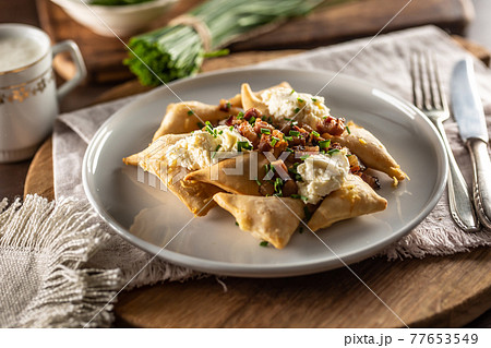 Fried pierogi served on a plate with bryndza cheese, bacon, and chives 77653549
