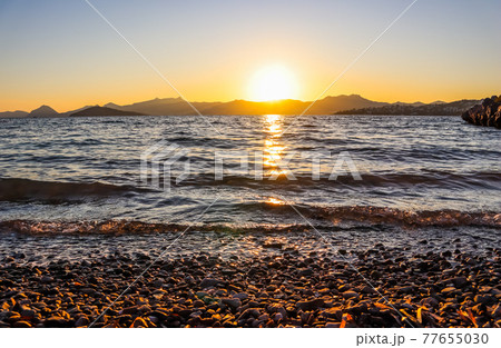 Beautiful sunset on the Mediterranean coast with islands and mountains. Stones on the beach lit by sunlight 77655030