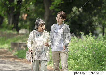 公園で散歩するシニア女性と介護士 77656182