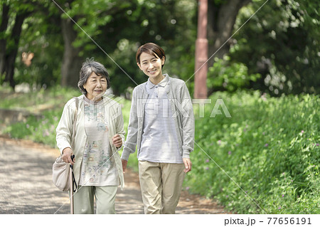 公園で散歩するシニア女性と介護士 77656191