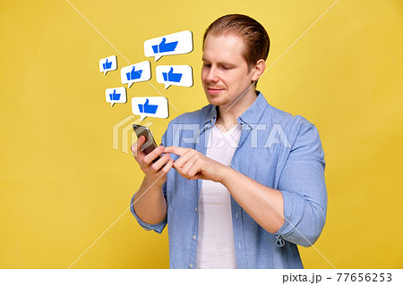 A man in a shirt on a yellow background looks like in a smartphone. Abstract icons with thumb up hanging in the air. A man in a shirt on a yellow background looks like in a smartphone. Abstract icons with thumb up hanging in the air. 77656253