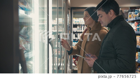 Young couple taking frozen food from fridge in the shop Young couple taking frozen food from fridge in the shop 77656725