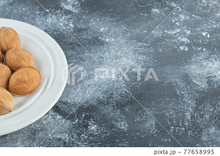 A white plate full of sweet walnut shaped cookies A white plate full of sweet walnut shaped cookies 77658995