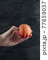 Holding a red peach and tapping on it on black background 77659037