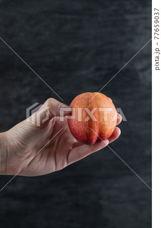 Holding a red peach and tapping on it on black background 77659037