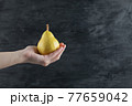 A person holding a yellow pear in the palm 77659042