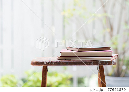 窓辺の木製脚立の上に積み重ねられた読み古された本 77661879