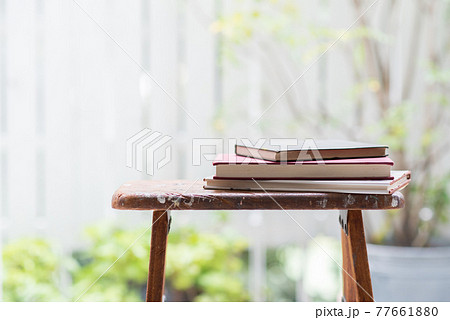 窓辺の木製脚立の上に積み重ねられた読み古された本 77661880