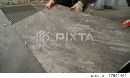 Adhesive solution for gluing ceramic floor tiles. Professional worker gluing decorative tiles to the floor. Industrial scale mortar application for gluing tiles to floors. 77662465