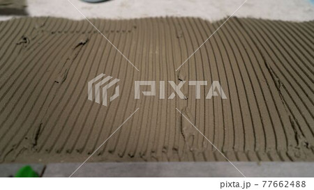 Tile adhesive applied to the floor for laying ceramic tiles. Dark grey ceramic floor tiles laid on applied adhesive. Tile adhesive applied to the floor for laying ceramic tiles. Dark grey ceramic floor tiles laid on applied adhesive. 77662488