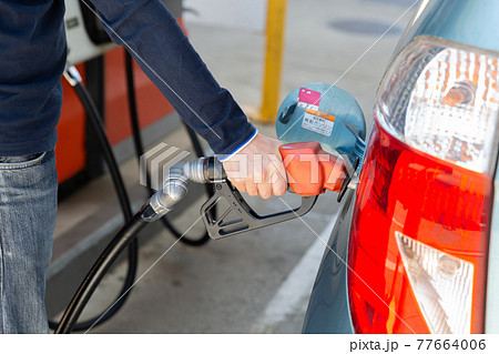 ガソリンスタンドのセルフサービスで車に給油する男性の手元 77664006
