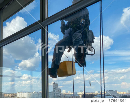 Outside of the building washing the glazing of the facade of a multi-storey building climbers clean windows Outside of the building washing the glazing of the facade of a multi-storey building climbers clean windows 77664364