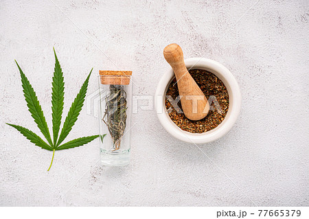 Glass bottle of cannabis oil with white mortar and hemp leaves set up on concrete background. Glass bottle of cannabis oil with white mortar and hemp leaves set up on concrete background. 77665379