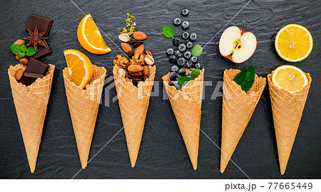 Various of ingredient for ice cream flavor in cones blueberry ,lime ,pistachio ,almond ,orange ,chocolate ,vanilla and coffee set up on dark stone background . Summer and Sweet menu concept. 77665449