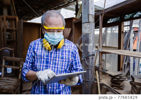 asian senior man carpenter wear headphone using tablet standing in workplace. carpenter concept. 77665829