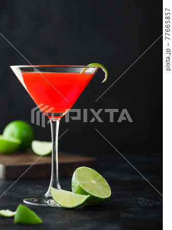 Cosmopolitan cocktail in classic crystal glass with lime peel and fresh limes on black background. Cosmopolitan cocktail in classic crystal glass with lime peel and fresh limes on black background. 77665857
