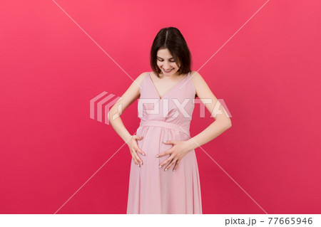Happy pregnant woman touching her abdomen at Colored background. Future mother. Expecting of a baby. Copy space Happy pregnant woman touching her abdomen at Colored background. Future mother. Expecting of a baby. Copy space 77665946