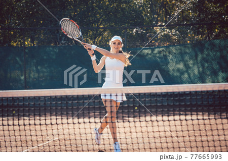 Woman forcefully playing tennis close to net 77665993