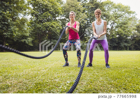 Smiling young women doing battle rope exercise in park 77665998
