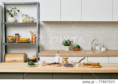 A kitchen with a shelf full of kitchenware and wooden table with food A kitchen with a shelf full of kitchenware and wooden table with food 77667025
