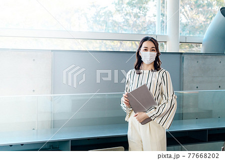 オフィスでマスクをしたパソコンを持った若い女性エンジニア オフィスでマスクをしたパソコンを持った若い女性エンジニア 77668202