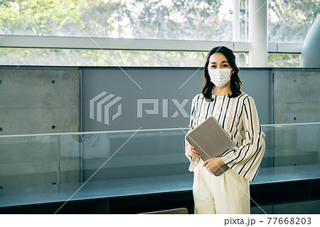 オフィスでマスクをしたパソコンを持った若い女性エンジニア オフィスでマスクをしたパソコンを持った若い女性エンジニア 77668203