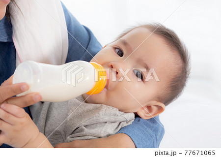 Young asian mother embracing and feeding little baby girl with bottle of milk at home. Young asian mother embracing and feeding little baby girl with bottle of milk at home. 77671065