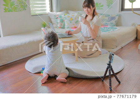 テーブルに手を掛ける乳児とコーヒーカップを持つテレワークの母親 テーブルに手を掛ける乳児とコーヒーカップを持つテレワークの母親 77671179