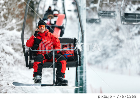 Skier sitting at ski lift talking on the phone in high mountains during sunny day. Winter sport and recreation, leisure outdoor activities. Skier sitting at ski lift talking on the phone in high mountains during sunny day. Winter sport and recreation, leisure outdoor activities. 77671568