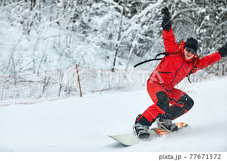 Male snowboarder in a red suit rides on the snowy hill with snowboard, Skiing and snowboarding concept Male snowboarder in a red suit rides on the snowy hill with snowboard, Skiing and snowboarding concept 77671572