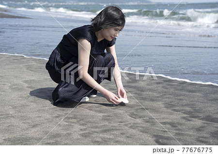 砂浜で貝殻を拾う若い女性の写真素材