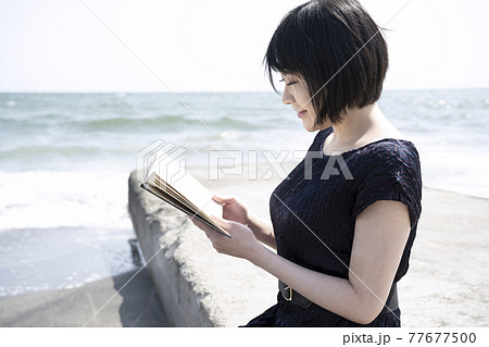 海岸の波止で本を読む若い女性 神奈川県鎌倉市七里ガ浜 の写真素材