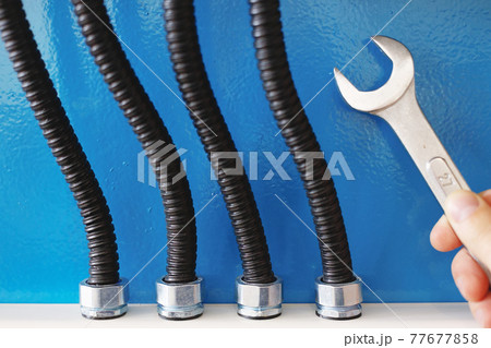 These are power cables in corrugated insulation and a rock electrician with a wrench close up against a blue wall 77677858