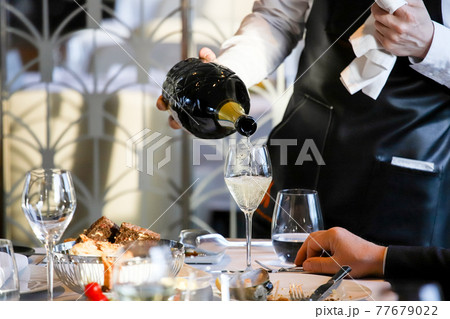 The waiter pours white wine into a glass. Banquet, cutlery, table setting. The waiter pours white wine into a glass. Banquet, cutlery, table setting. 77679022