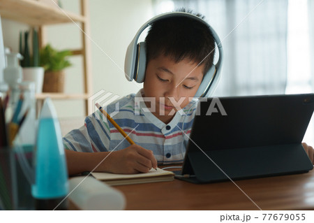 Asian boy learning online via internet with a tutor on a tablet digital with headphone Asian boy learning online via internet with a tutor on a tablet digital with headphone 77679055