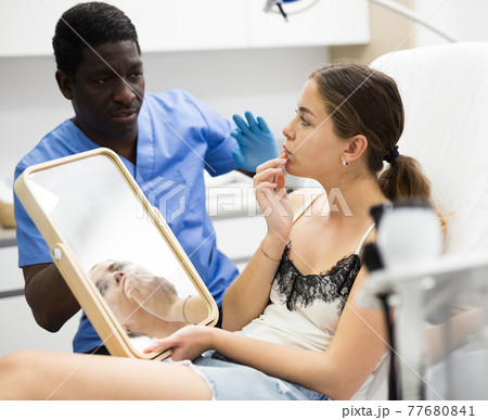 Female client looking at mirror while beautician examining her face Female client looking at mirror while beautician examining her face 77680841